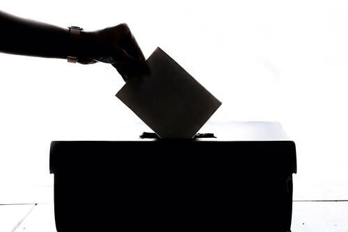 Svart kvitt foto av hand som held på å putte ein stemmeseddel ned i ei valurne. 